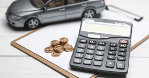 Calculator, coins and a toy car on a clipboard, symbolising car loans and vehicle financing calculations.
